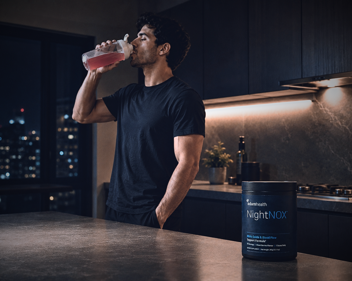 A man drinking NightNOX from a shaker in a dark kitchen at night, with the tub on the counter.